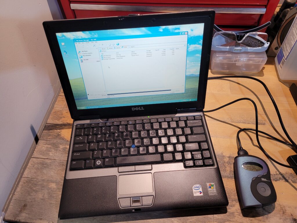 Dell laptop on a desk with a Rio600 mp3 player connected to it.